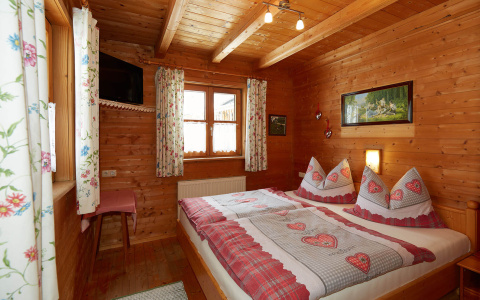 Gemütliches Schlafzimmer in Almhütte Wagrain aus Holz, Doppelbett, Herz-Bettwäsche, Berghütte