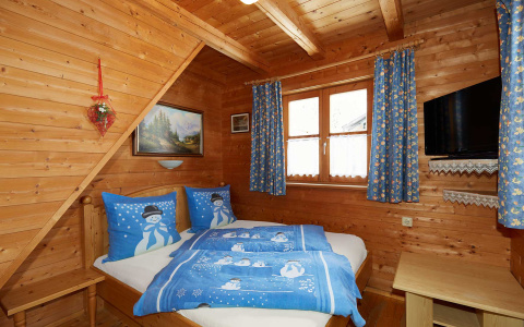 Gemütliches Schlafzimmer mit Holzwänden, Doppelbett, blauer Schneemann-Bettwäsche und TV